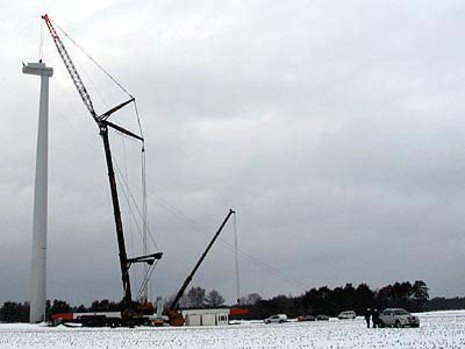 Ein Kran montiert die Turbine an einer Windkraftanlage, die auf einem verschneiten Feld errichtet wurde.