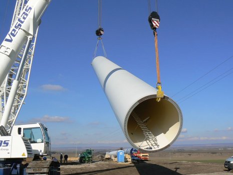 Der Mast einer Windkraftanlage wird von einem weißen Kran angehoben.