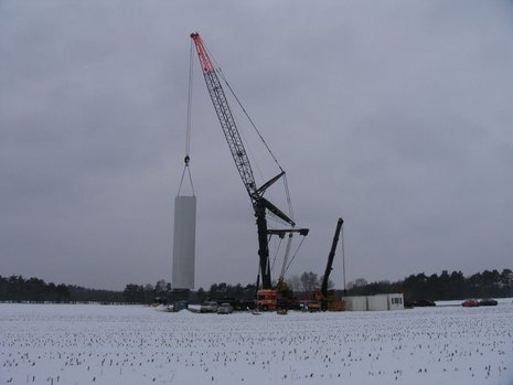 Ein Kran hebt den Mast einer Windkraftanlage in die Höhe.