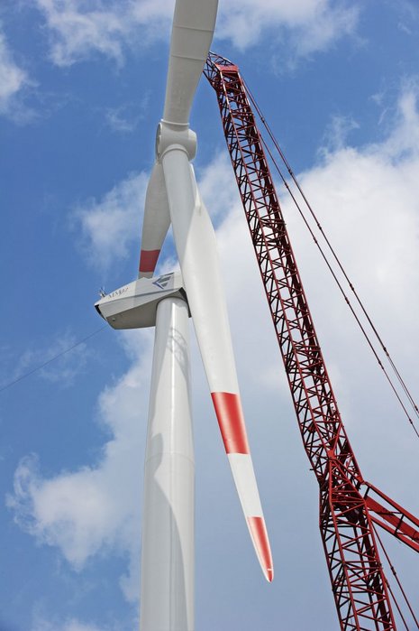 Foto von unten von der Montage der Windturbinenflügel mithilfe eines roten Krans.