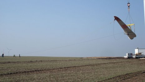Ein Windradblatt wird über einem Feld in die Luft gehoben.
